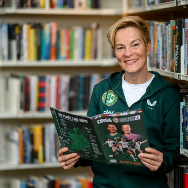 Woman leaning on bookshelves holding a book and smiling