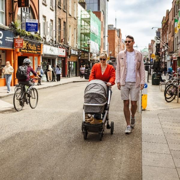 woman and man walking on pedestrian street, pushing a child in a pram